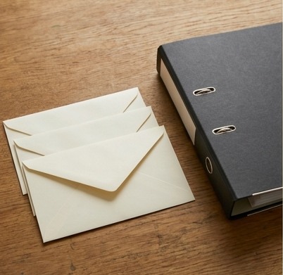AI-generated editorial illustration: ivory envelopes and charcoal binder.