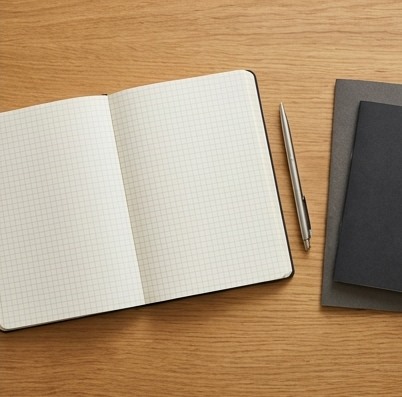 AI-generated editorial illustration: blank grid notebook beside charcoal folder.